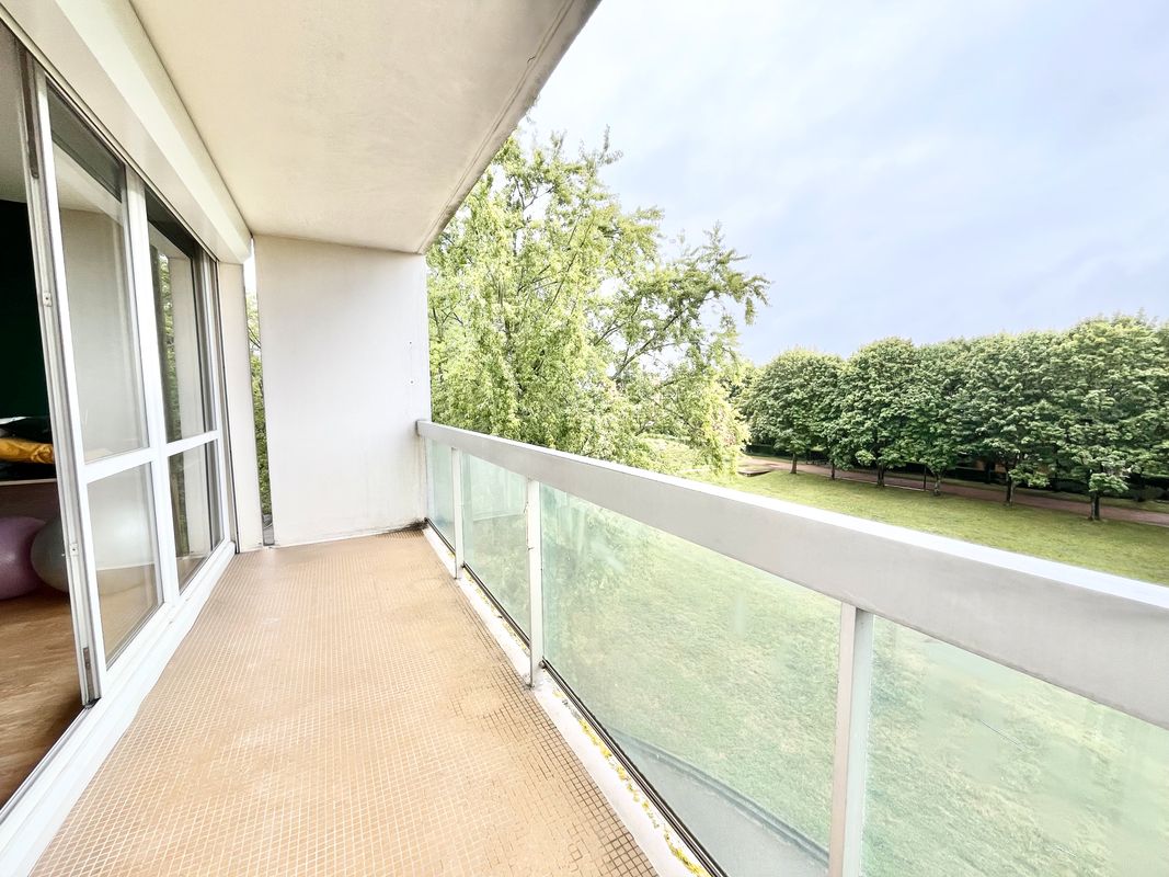 Balcon spacieux avec garde-corps en verre et vue dégagée sur un parc arboré