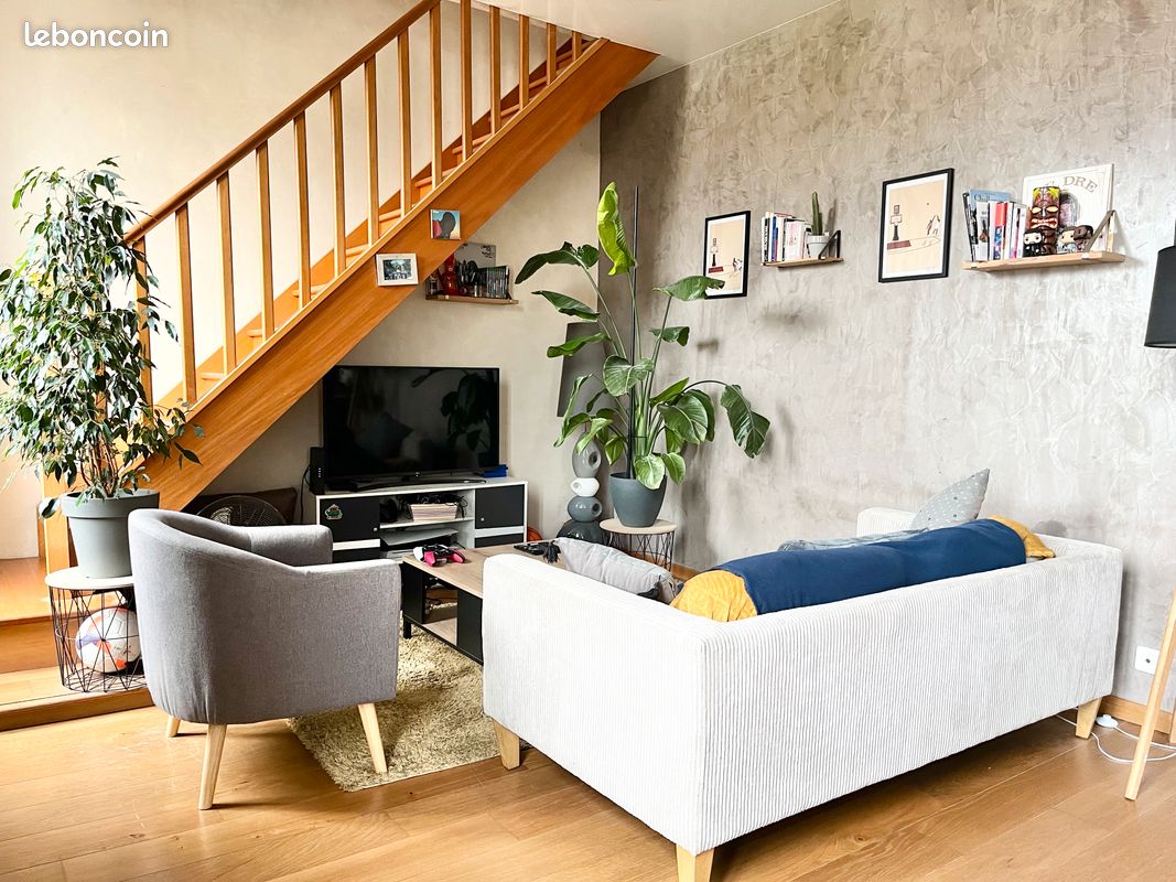 Salon cosy avec canapé, fauteuils et un escalier en bois menant à l'étage.