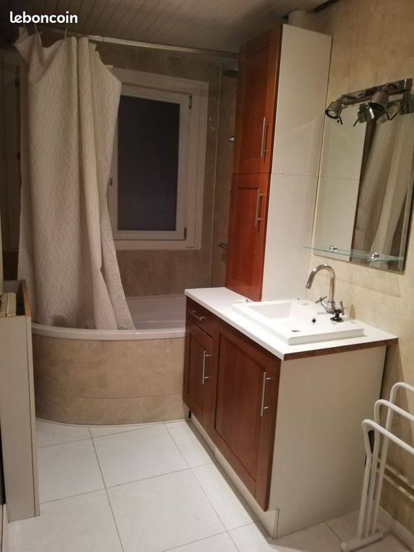 Salle de bain avec baignoire d'angle, meuble en bois et miroir éclairé.