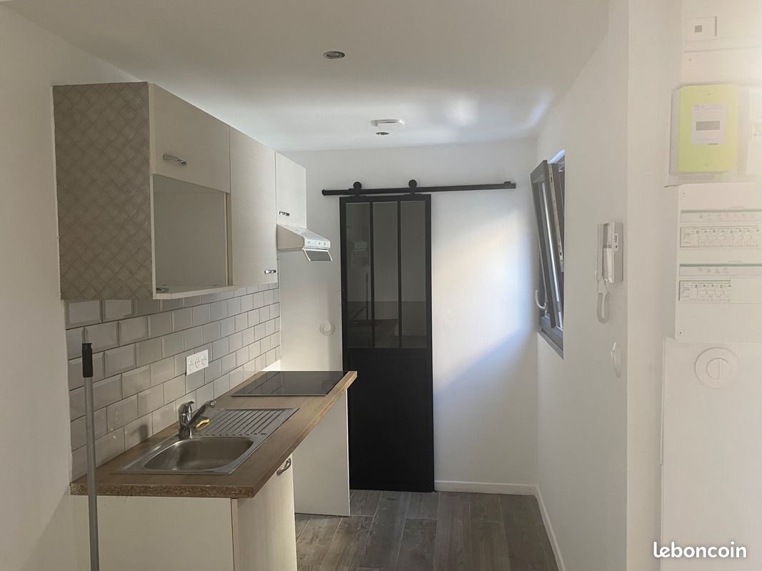 Studio Montreuil 25 m², Cuisine compacte avec crédence en carrelage métro et porte coulissante noire.