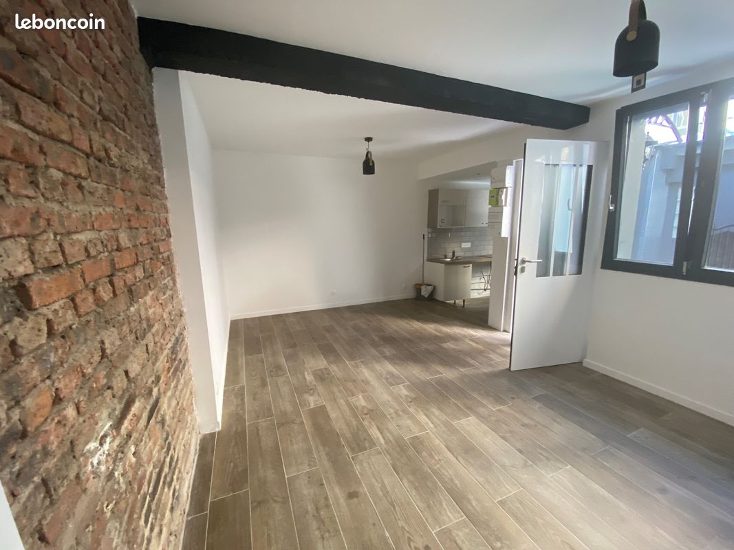 Studio Montreuil 25 m², Pièce principale avec mur en briques apparentes et poutres noires.