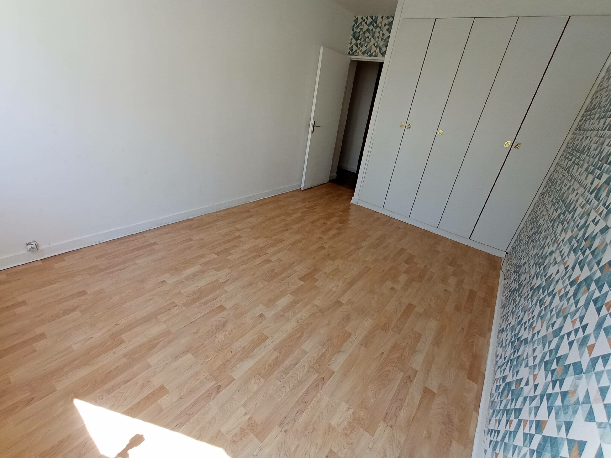 Chambre 3 vue avec les placards, parquet au sol et papier peint sur un des murs